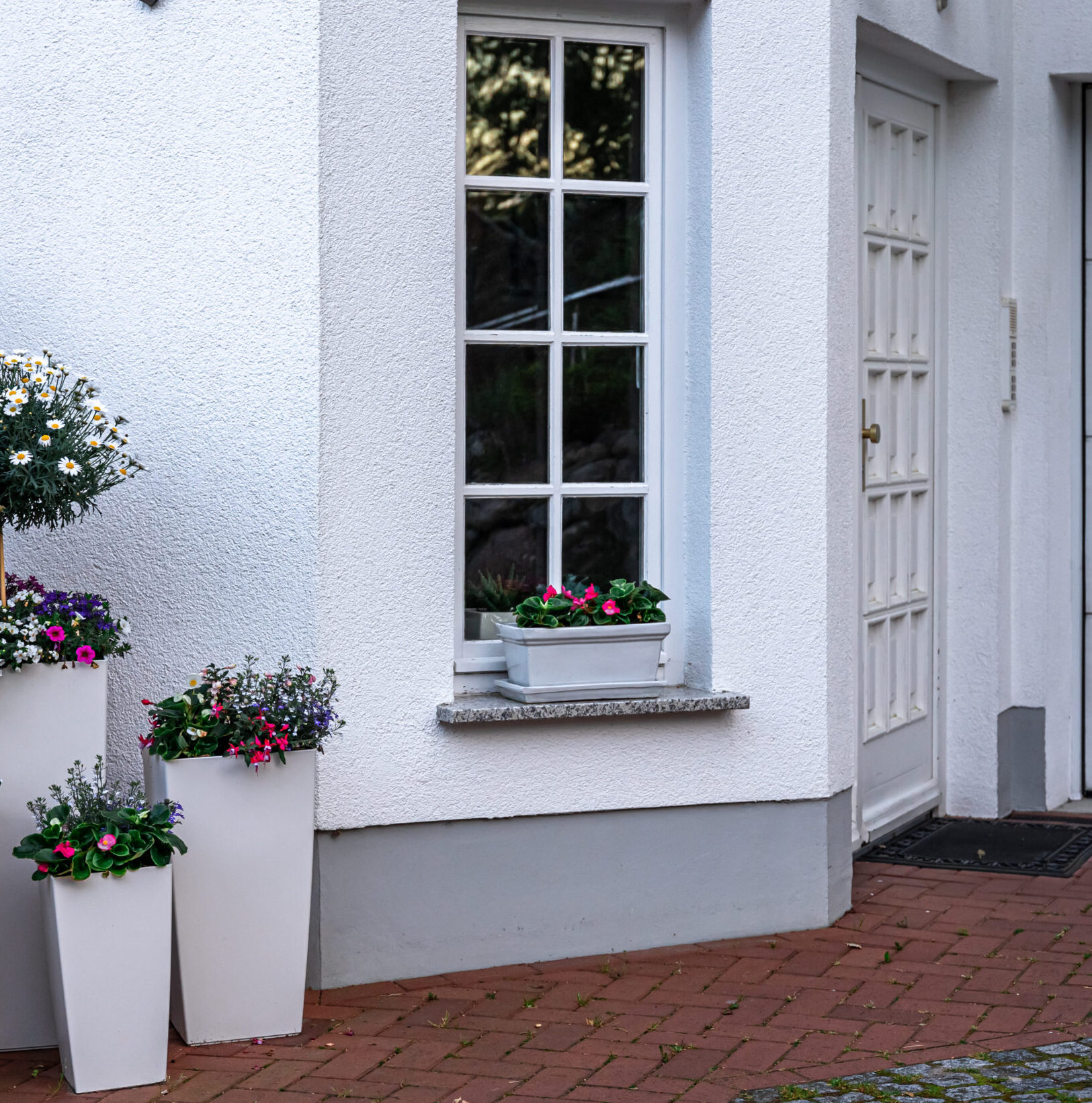 Part of the exterior of the house in white with flowers in pots for decoration.