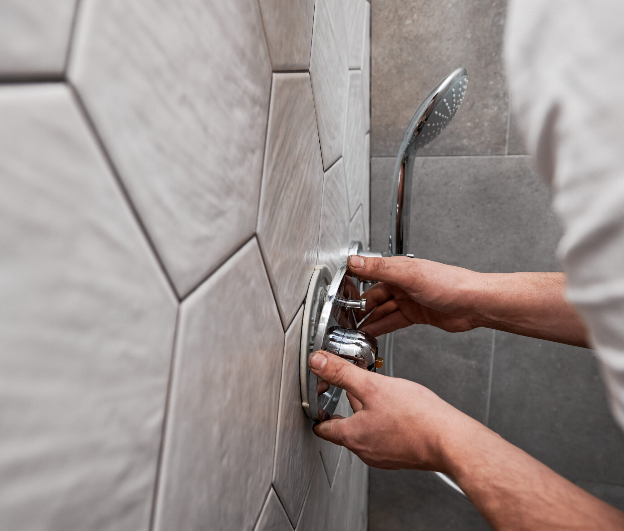 Close up of man standing by the wall with ceramic tile and installing shower faucet with metal handle in apartment. Male plumber working on bathroom renovation at home. Plumbing works concept.