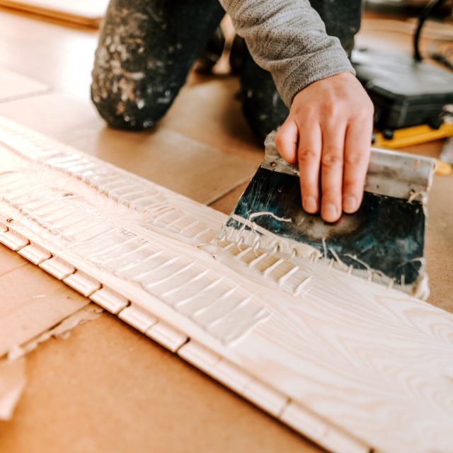 Worker laying and gluing parquet flooring. Worker installing hardwood flooring during house building and construction